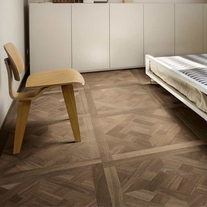 Wooden chair and bed against a wall with white cabinets on a wood effect tiled floor.