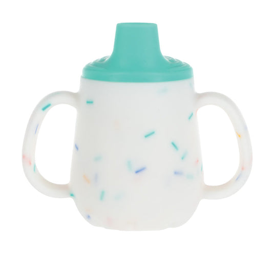 The 2-Handle First Training Cup | Aqua Confetti is a white silicone cup with colorful sprinkles, teal free-flow spout lid, and two easy-grip handles, designed for young children. Shown on a plain white background.