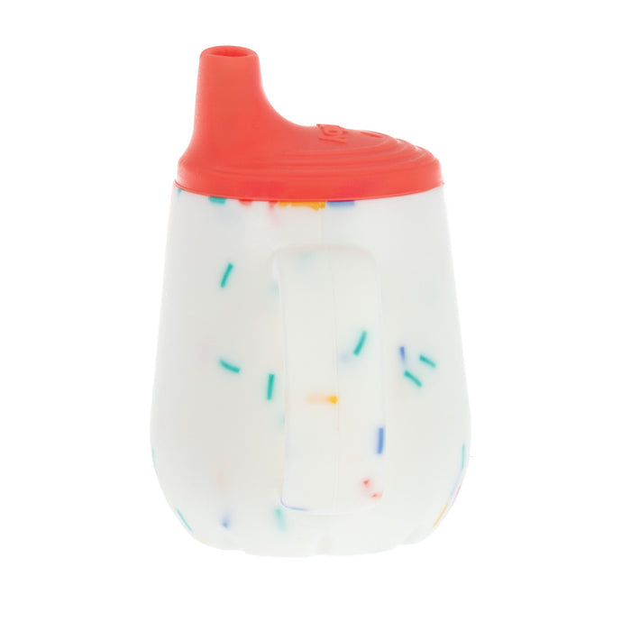 The Nuby US 2-Handle First Training Cup | Red Confetti features a white body with colorful confetti patterns, a red free-flow spout lid, and side handles, shown against a plain white background.