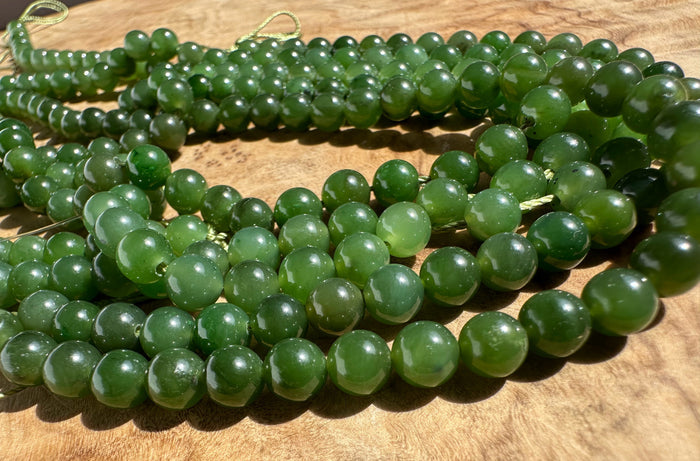 Multiple strands of polished green gemstone beads arranged on a wooden surface.