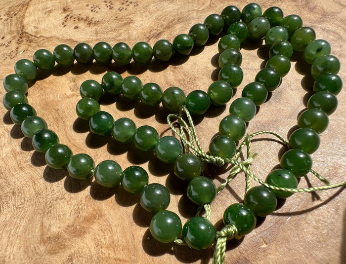 A strand of polished dark green jade beads with a matching green cord, arranged on a textured wooden surface.