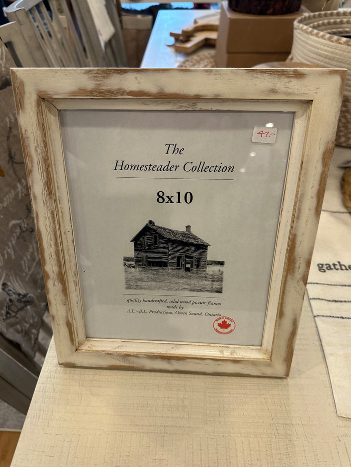 An 8x10 picture frame with a white distressed finish, displaying a black and white photo of a house. The frame has a label that reads 'The Homestead Collection' and '8x10'.
