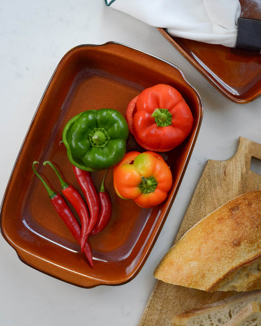 Ceramic stoneware baking dish with peppers and chilies on a white marble surface with bread.