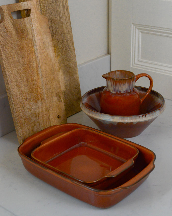 Set of brown ceramic cookware including a bowl, pitcher, and rectangular dish on a white surface.