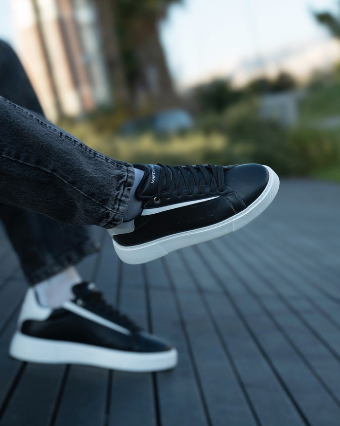 Martin Valen Axino men's black casual sneakers with white details, side view on foot showing tongue logo and thick white sole