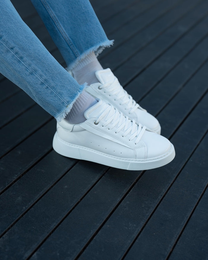 Martin Valen Axino men's casual white sneakers worn with blue jeans, front on-foot view on a dark wooden deck