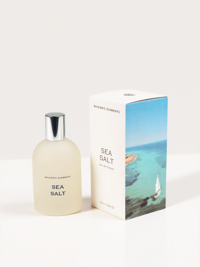 A frosted glass bottle of Balearic Elements Sea Salt Eau de Toilette next to its white packaging box featuring a blue ocean and sailboat illustration, on a clean white background.