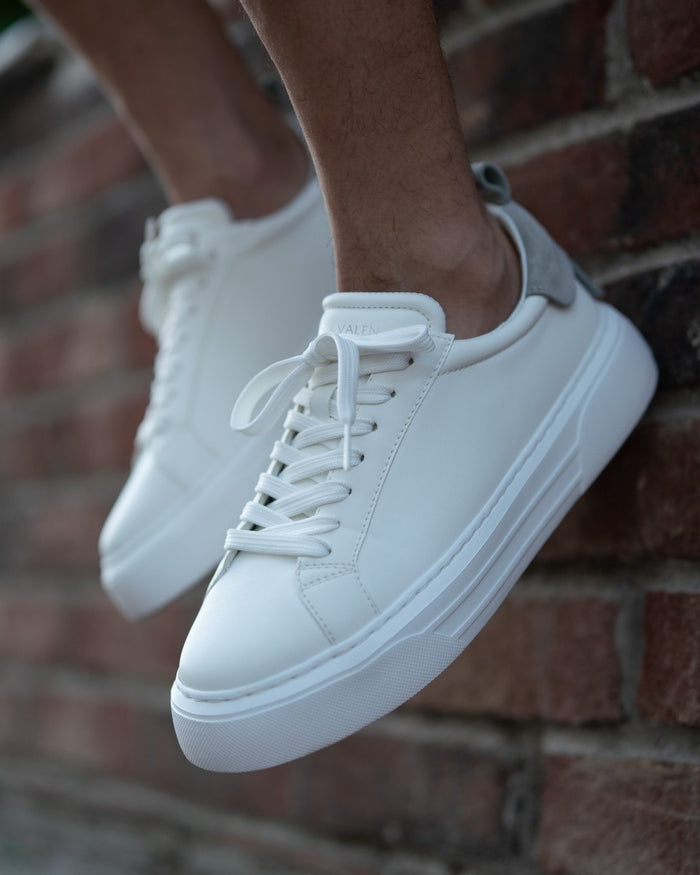 Martin Valen Bobe Suede Belted white and grey sneakers, front-angled on foot by a brick wall showing laces and thick platform sole