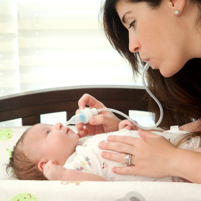 A woman gently uses the Breathe-eez Nasal Aspirator to relieve her baby's congestion while the baby lies on a changing table, looking up.