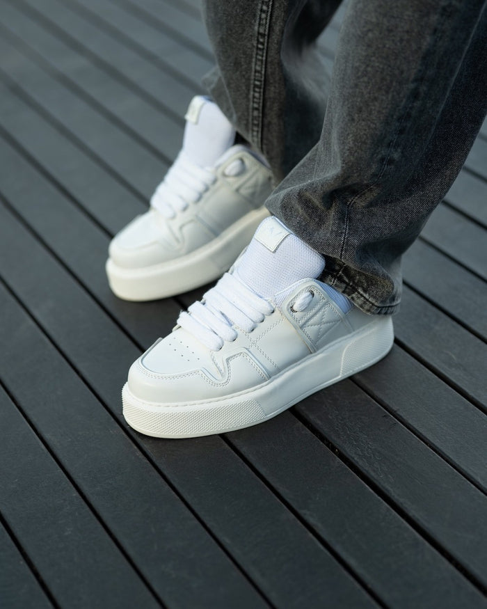 Martin Valen bulky white sneakers, three-quarter view showing laces and thick platform sole, worn with grey jeans.
