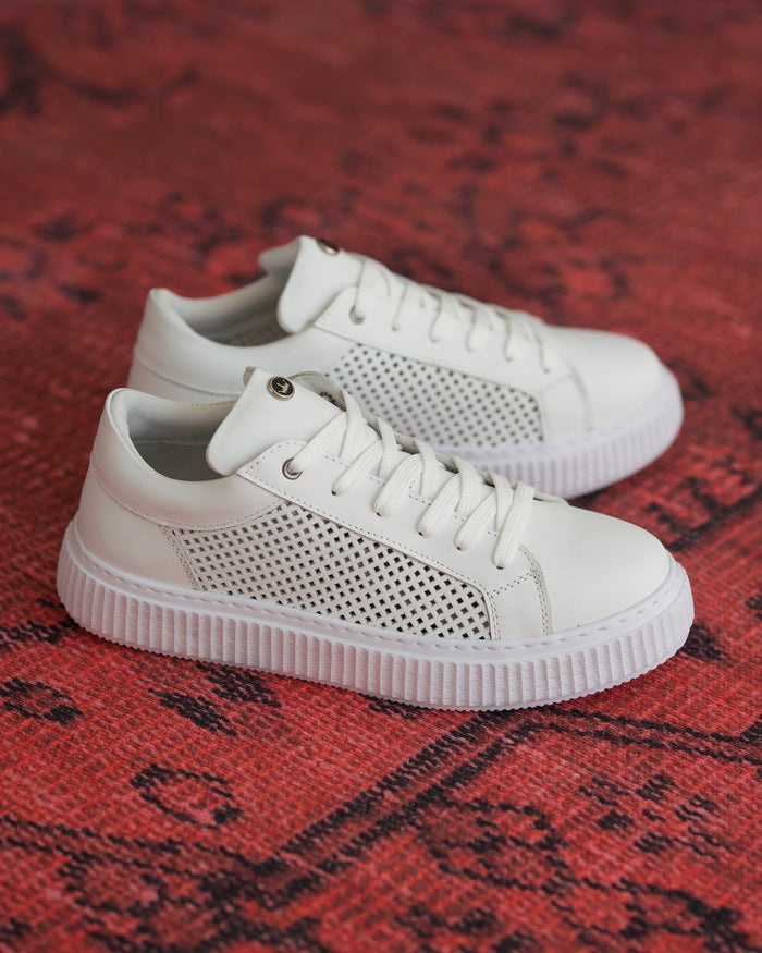 Martin Valen white leather mesh sneakers, three-quarter view on red rug showing laces, perforated side panel and sole