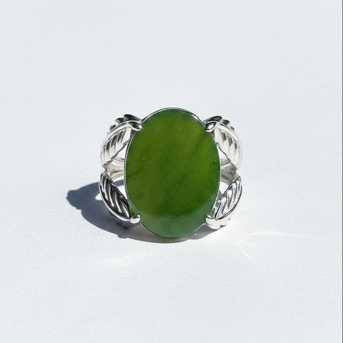 A silver ring with a large oval green jade, photographed on a white in natural sunlight.