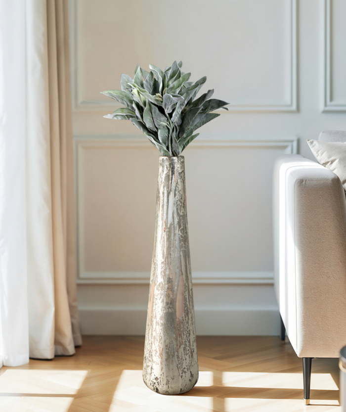 Tall narrow metallic vase with greenery in a living room.