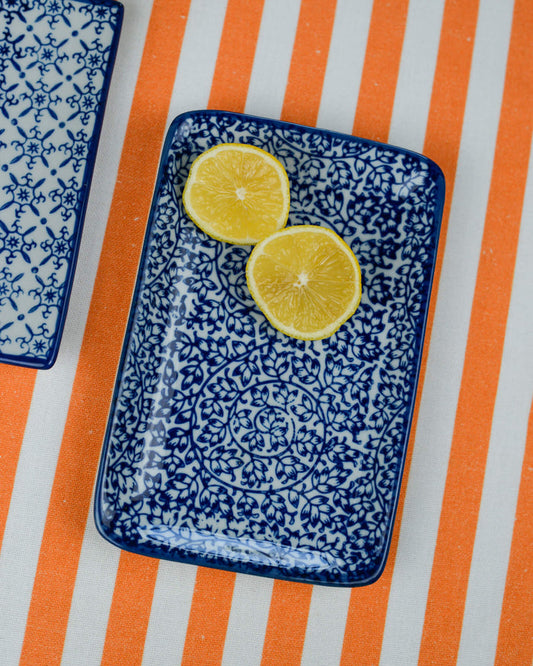 Two lemon slices on a blue patterned rectangular plate with an orange and white striped table runner underneath.