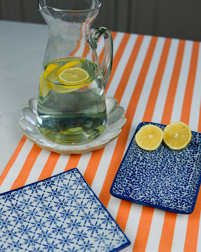 Clear pitcher with lemon slices on a striped tablecloth with two decorative side plates
