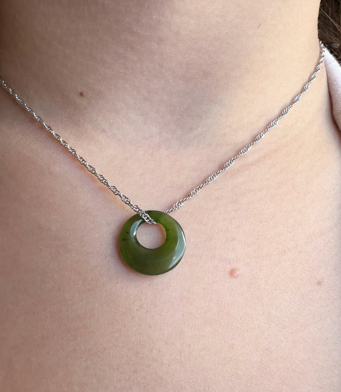 A close-up of a person's neck and chest wearing a silver chain necklace with a green circular pendant.