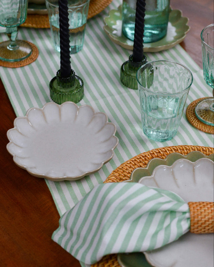 Table setting with green and white striped table runner, white plates, and decorative napkins.