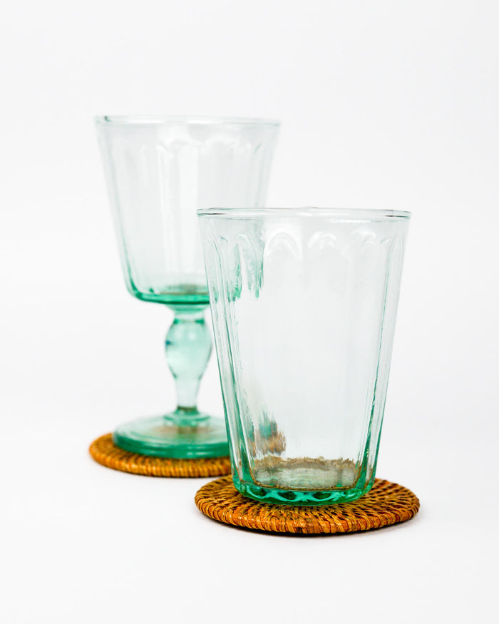 Two green glass tumblers on rattan woven coasters with a white background