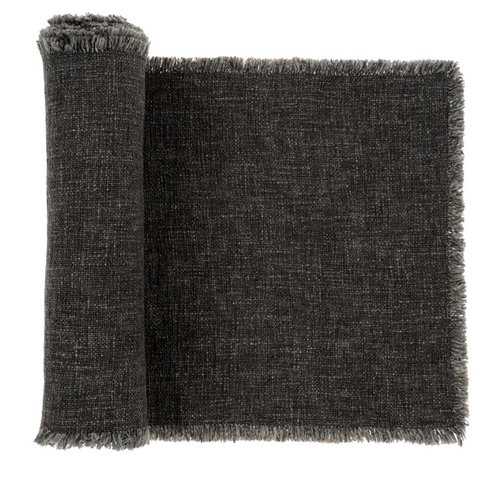 A dark grey linen table runner with a textured fringe, folded over the edge of a table.