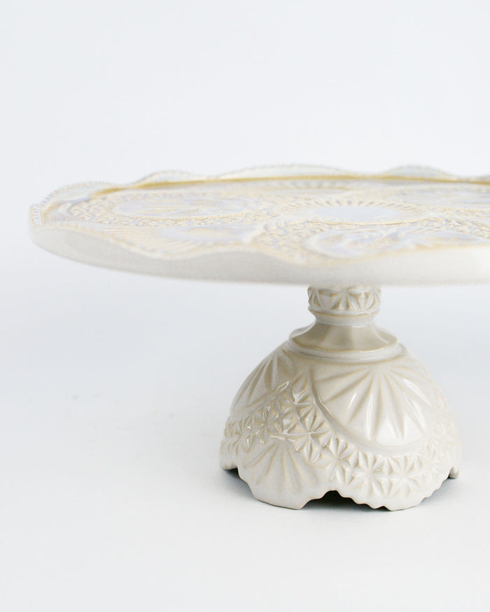 Decorative white cake stand with intricate patterns on a white background