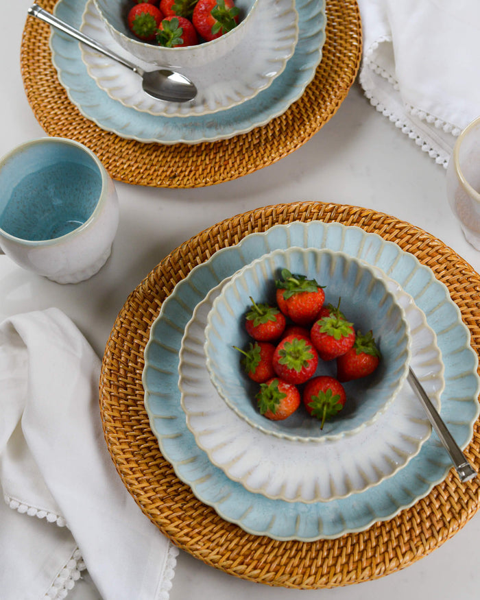 Ceramic stoneware salad and dinner plates with a scalloped edge on a woven placemat