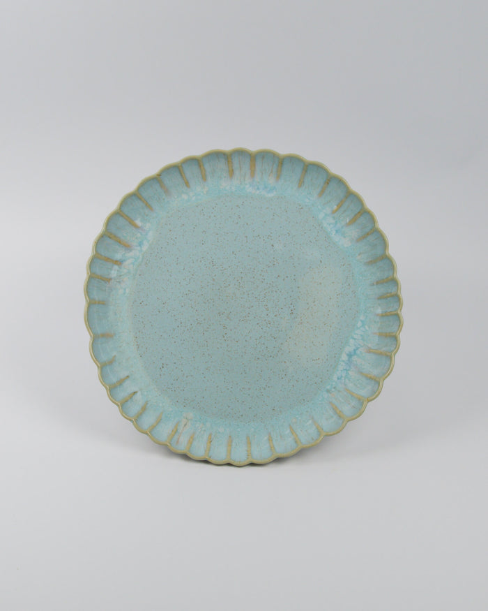 Light blue ceramic stoneware dinner plate with scalloped edge on a white background