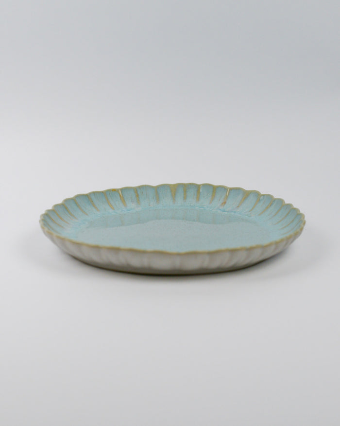 Light blue ceramic dinner plate with a textured edge on a white background