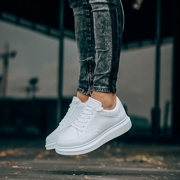 Pair of Martin Valen men's white sneakers suspended mid-air, three-quarter front view showing chunky sole and perforations