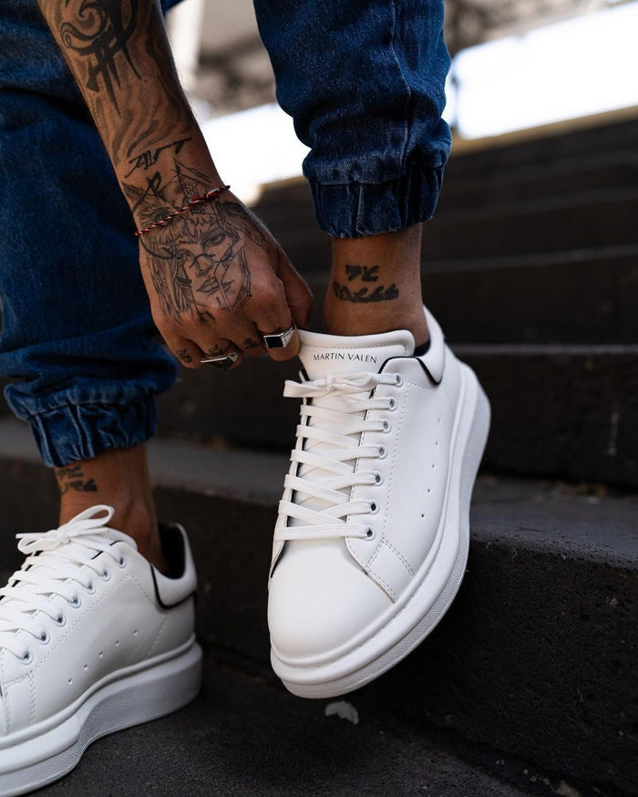 Martin Valen men's chunky white sneakers with black line detail, model in cuffed blue jeans adjusting the shoe
