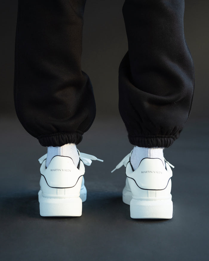 Martin Valen men's chunky white sneakers with black heel line, rear on-foot view showing branded heels and black jogger cuffs.