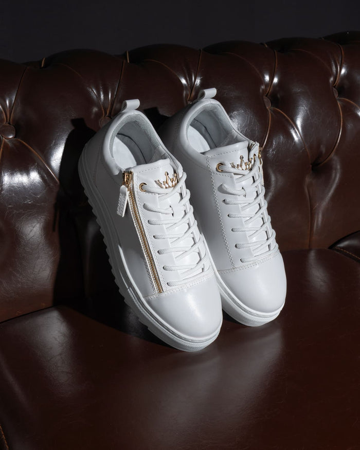 Martin Valen men's low-top white sneakers, angled top view on dark leather showing gold side zipper and crown eyelets
