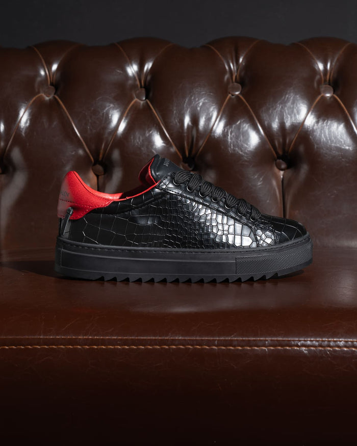 Martin Valen men's low-top black sneaker with crocodile embossing, profile shot on dark background highlighting serrated sole