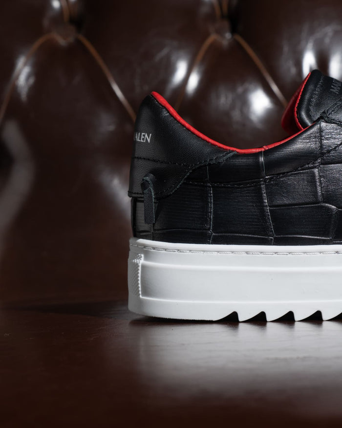 Close-up of Martin Valen black croc‑pattern sneaker with thick white platform sole and vivid red inner lining