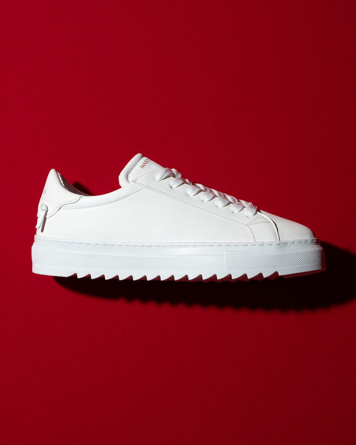 Martin Valen men's low-top white sneakers, side profile on red background showing chunky serrated sole.