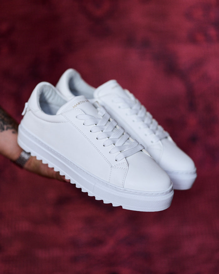 Martin Valen men's low-top white sneakers held at a three-quarter front angle, showing laces and ridged platform sole
