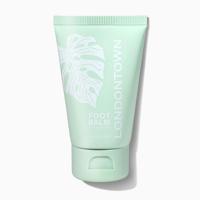 A mint-green tube labeled "LONDONTOWN Foot Balm" with a white leaf illustration stands upright on a white background, emphasizing its nourishing and soothing benefits for feet.