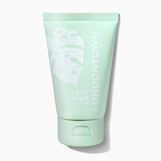 A mint-green tube labeled "LONDONTOWN Foot Balm" with a white leaf illustration stands upright on a white background, emphasizing its nourishing and soothing benefits for feet.