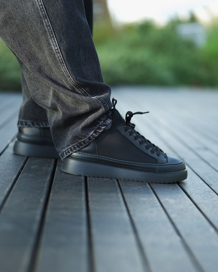 Martin Valen MonoFlux high-sole black scuba fabric sneaker, side view worn with grey jeans on a wooden deck