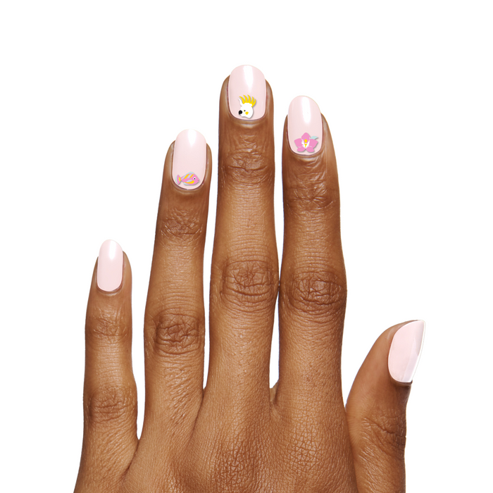 Hand with pale pink manicure and Nail Paradise stickers of tropical bird, flower, and fish on medium dark skin tone