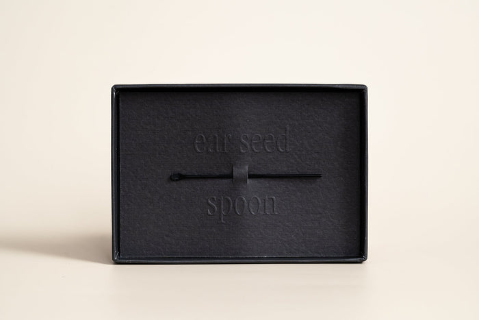 Black ear seed spoon tool resting inside a black box with embossed text, designed for use with Pain Conrol - 24K Gold Ear Seed | Vie Healing.