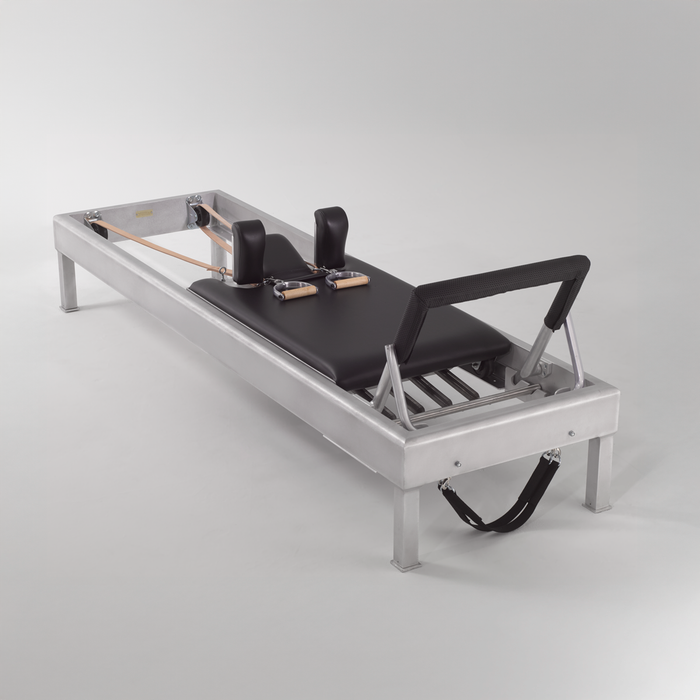 Gratz aluminum-frame Pilates reformer with black upholstery, shoulder rests, and leather handles.