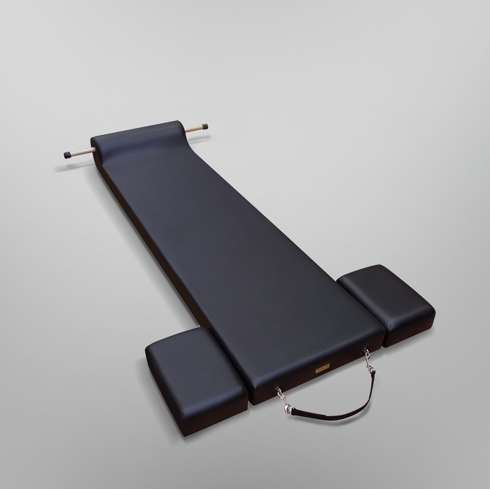 Black Gratz Pilates contour mat with wooden roll-up pole and leather carry strap.