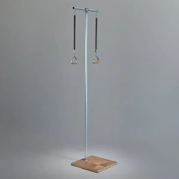 Pilates pole in silver with wooden square base, dual spring resistors, and hanging wooden stirrup handles.