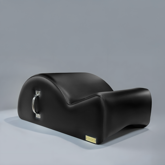 Black upholstered Gratz Pilates spine corrector with a chrome carry handle and brass plate.