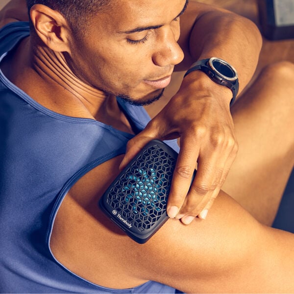 Man using RecoveryTherm Cube | Therabody in black on his shoulder for targeted muscle relief and wellness recovery care.