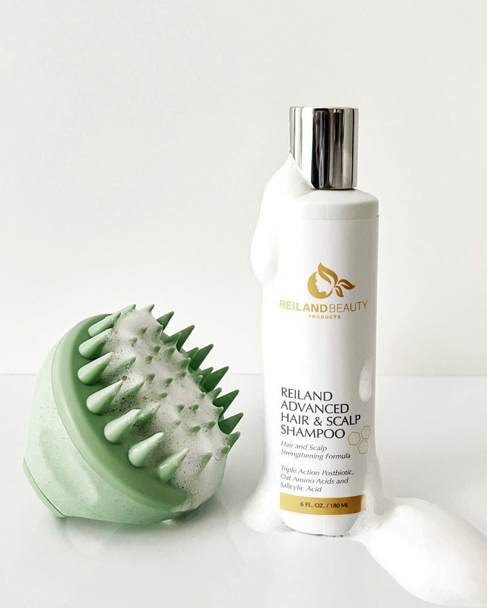 Reiland Advanced Hair & Scalp Strengthening Shampoo – 6 oz bottle with Triple Action Postbiotic formula, pictured with green scalp massager covered in luxurious foam. Designed to deeply cleanse, soothe scalp irritation, and promote healthy hair growth.