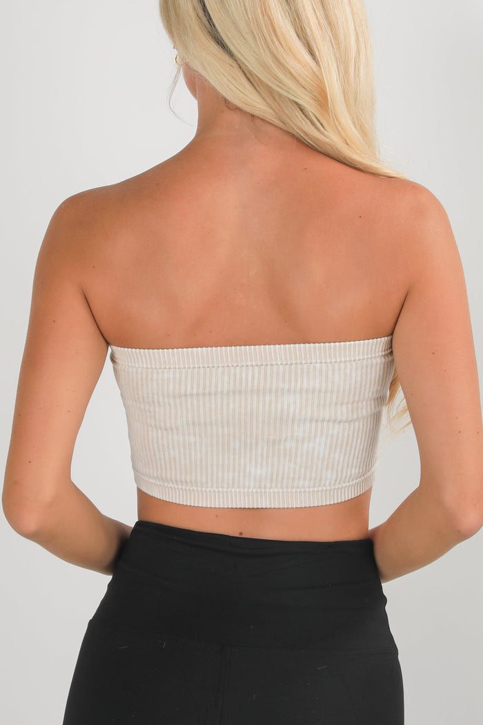 Woman wearing a strapless beige top and black pants on a plain background