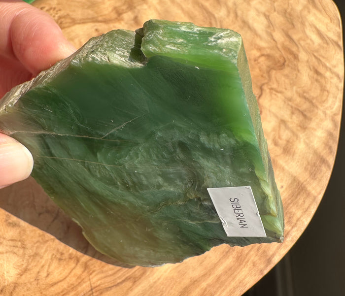 A hand holding a raw green stone slab labeled 'SIBERIAN' on a wooden surface.