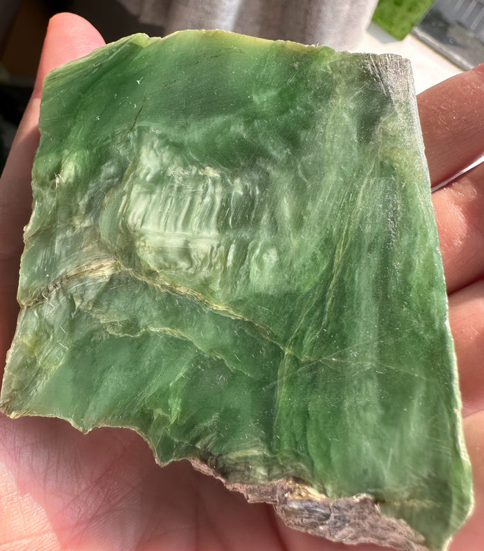 A raw green stone or mineral slab with natural striations and rough edges, held in a person's hand.