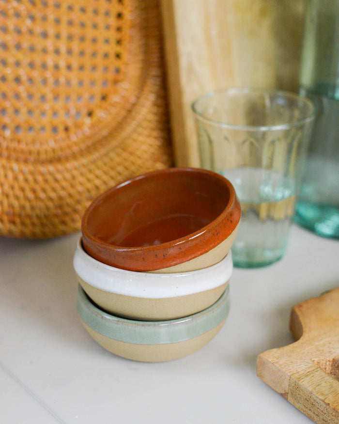 Stack of ceramic dipping bowls with a woven basket and glass in the background
